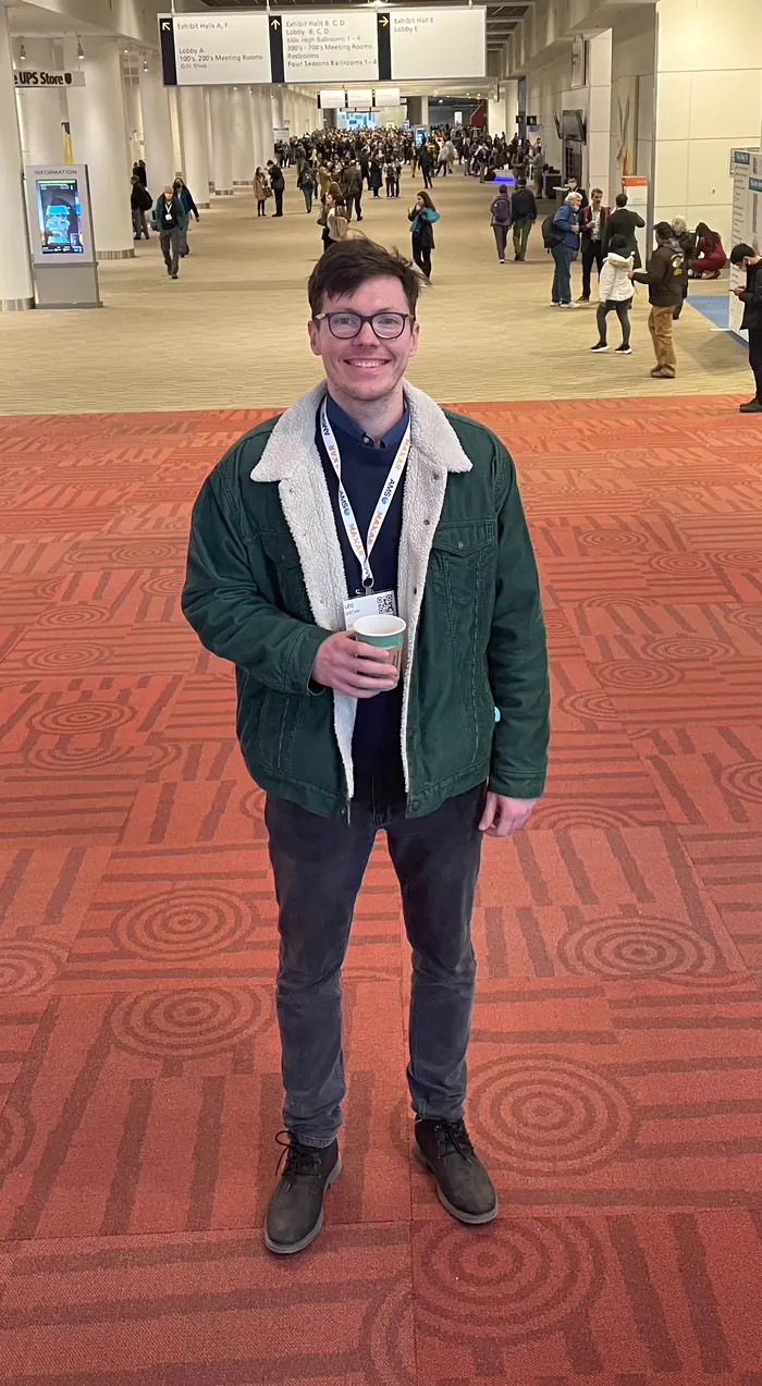 Leo at a conference centre, holding a coffee