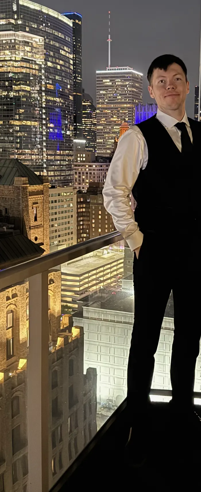 Leo on a balcony at night with the downtown Houston skyline behind him