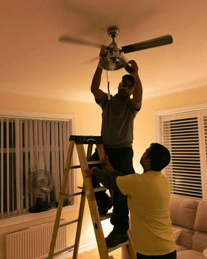 Electrician on a ladder fitting a ceiling fan in a living room