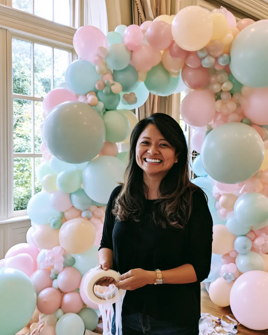 Gaby, the owner, standing in front of a pastel balloon arch she built