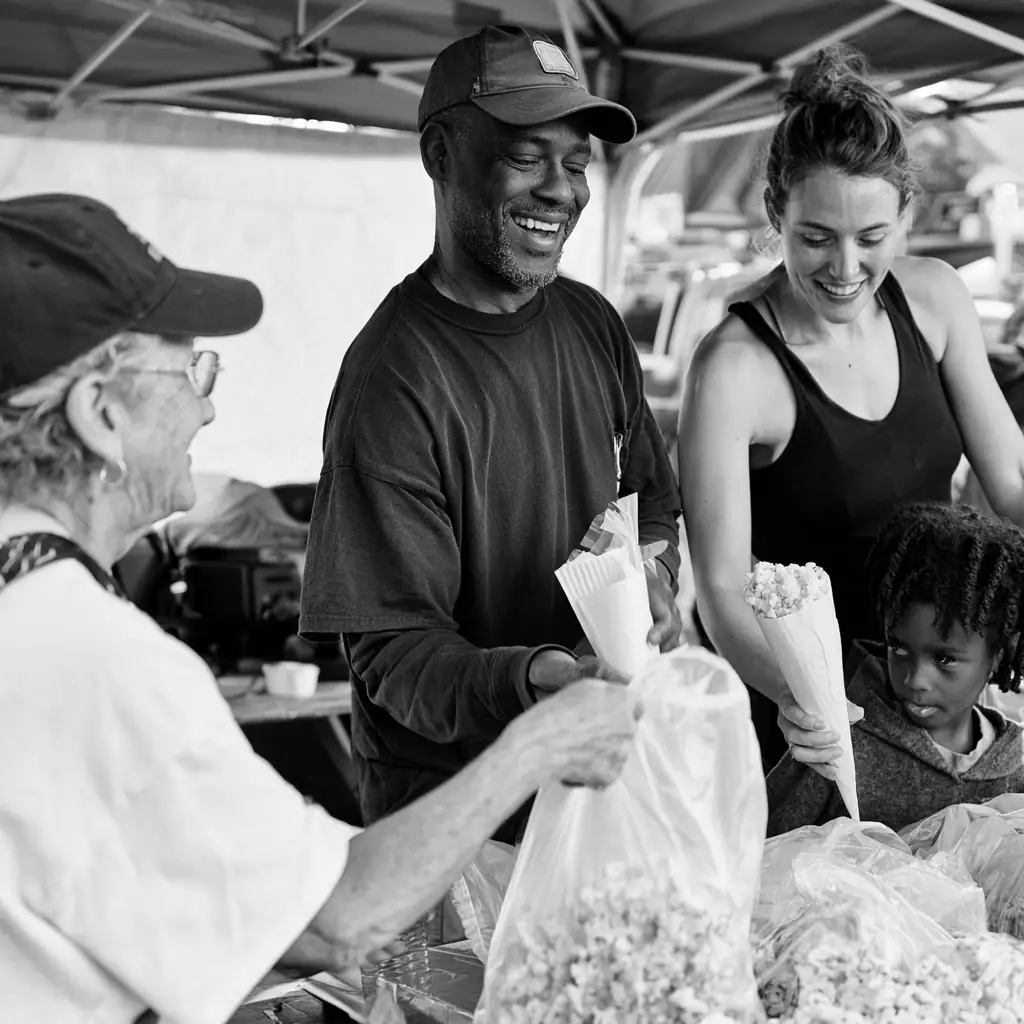 Black and white photo of the family handing bags to customers at the tent
