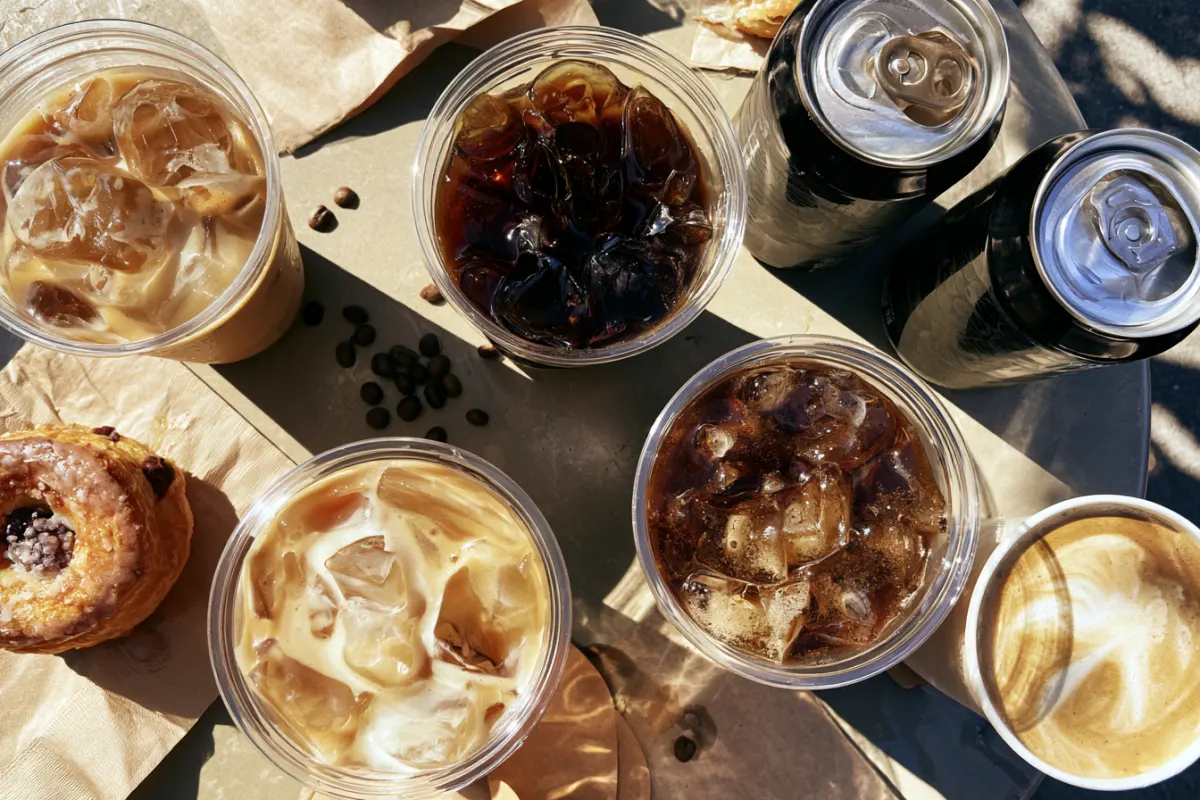 Iced lattes, cappuccinos, canned lattes and a pastry on a table, from above
