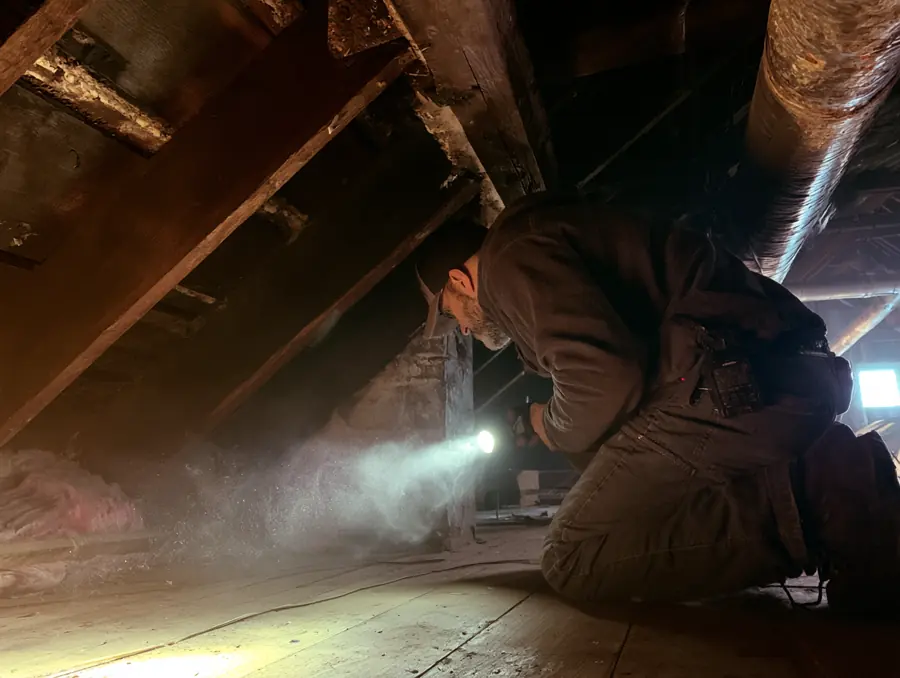 Technician inspecting an attic with a flashlight