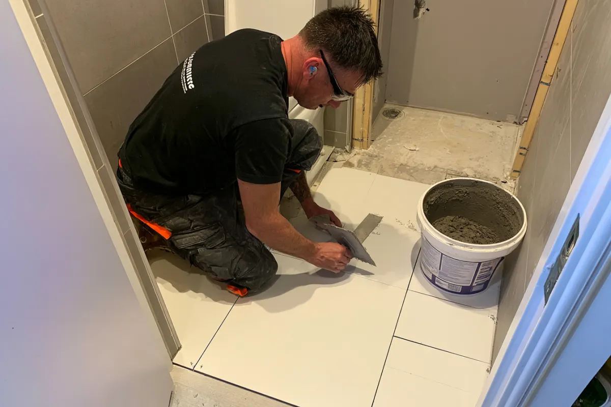 A tile installer setting large white floor tiles in a bathroom